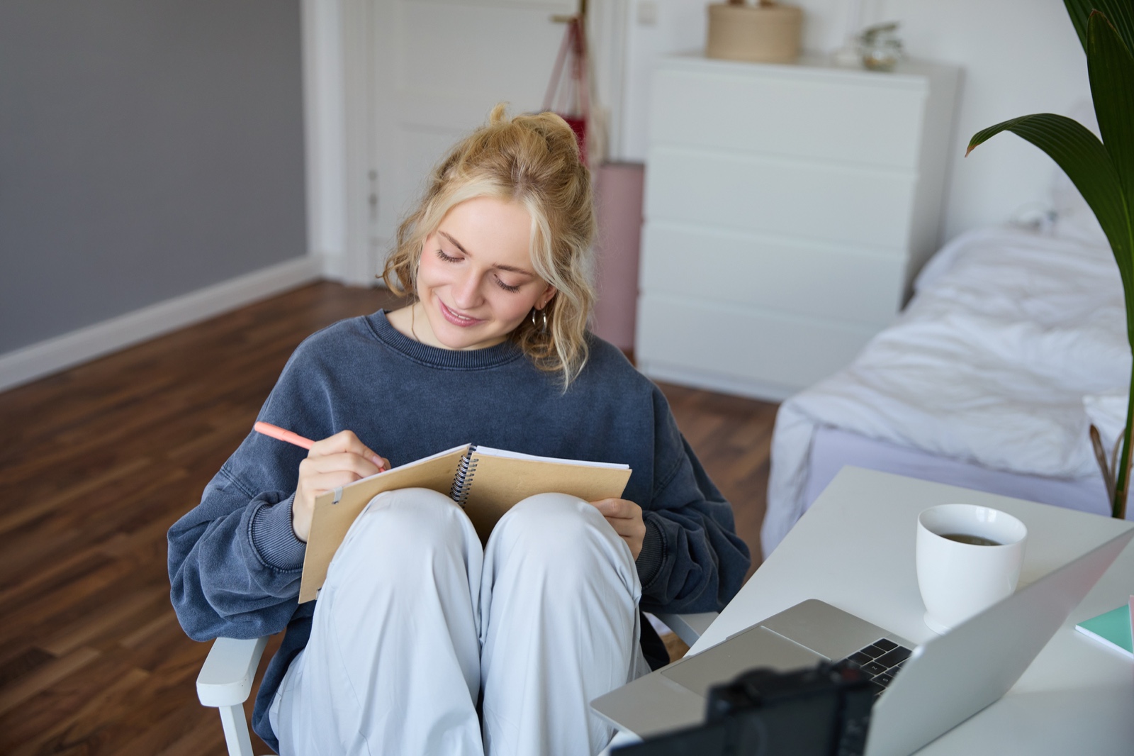 Creator writing in a notebook beside a laptop