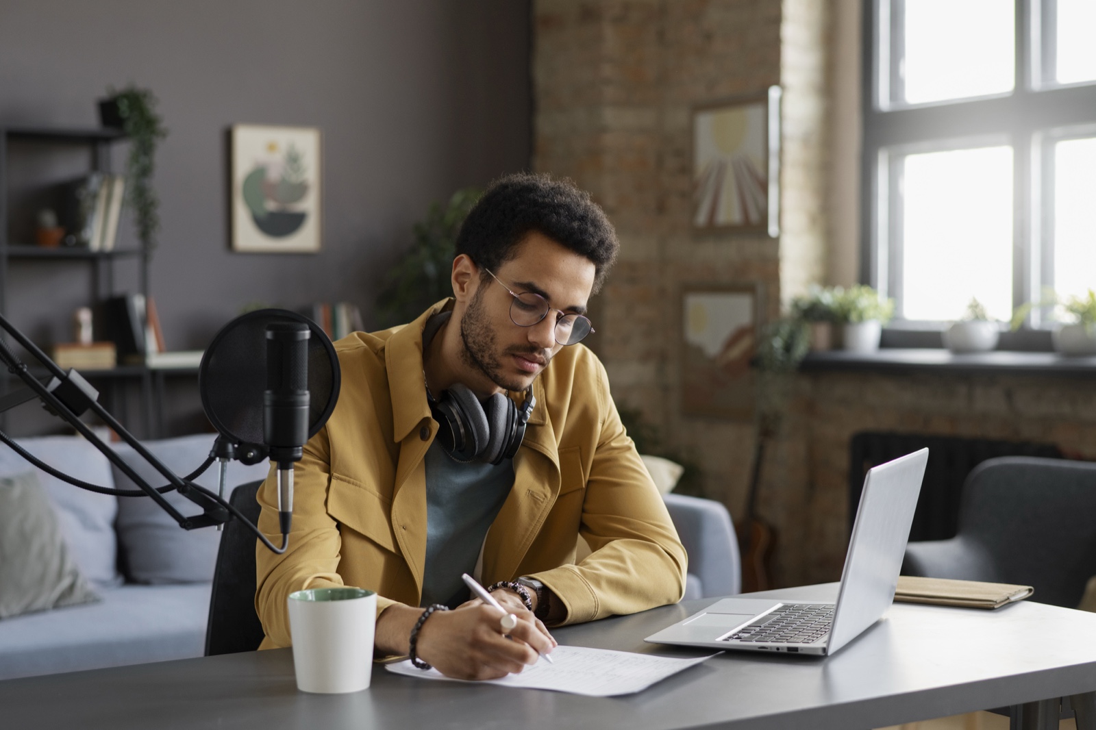Creator writing notes next to a microphone and laptop