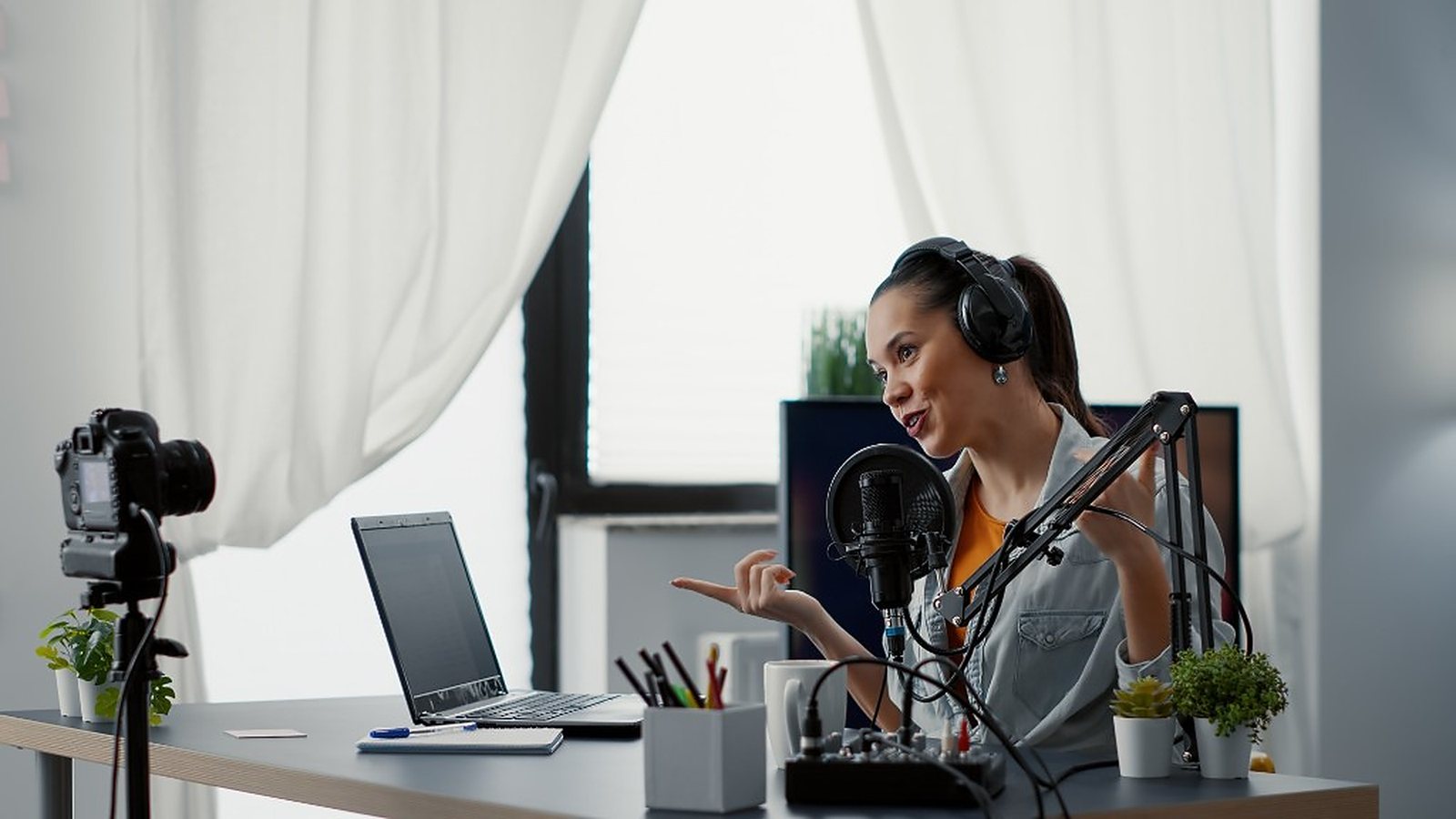 Creator speaking into a microphone in a bright home studio with camera and laptop
