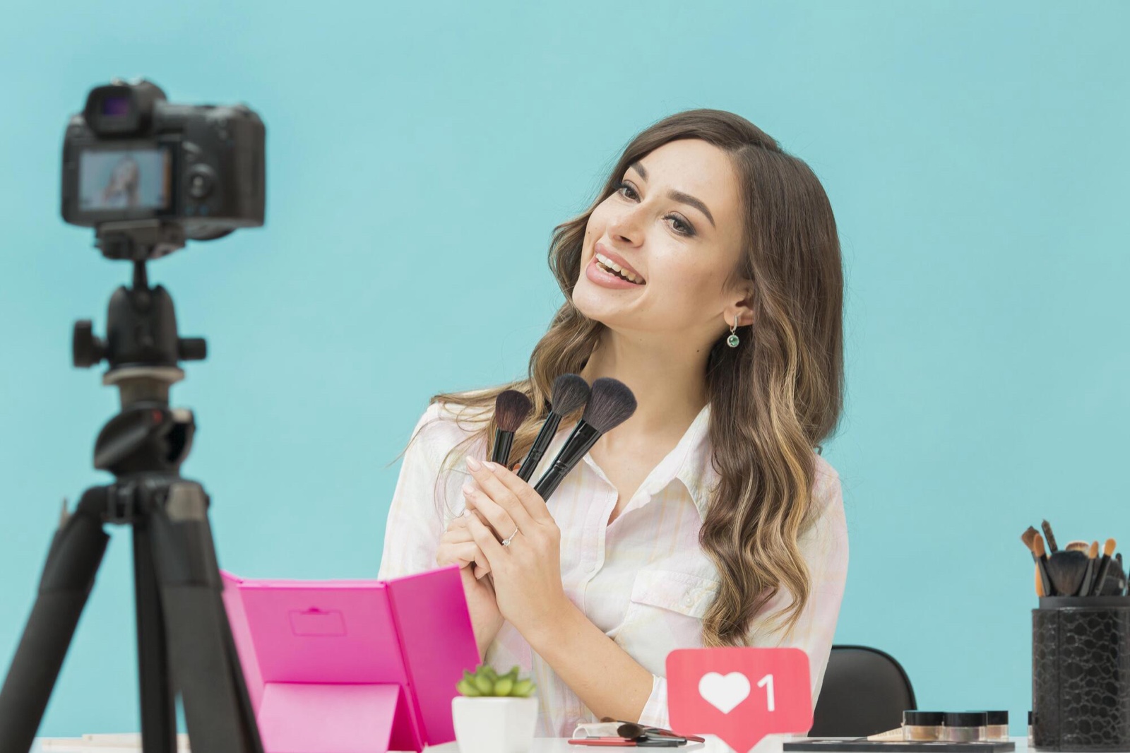 Creator holding makeup brushes beside a camera